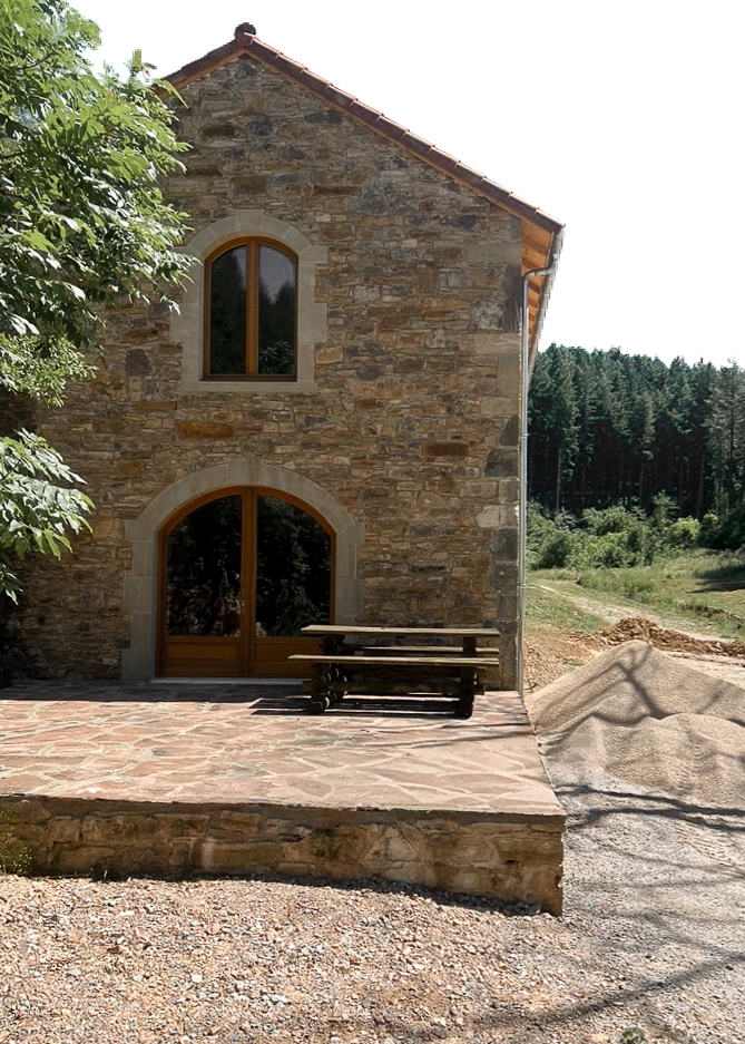 Grange en pierre réhabilitée sur le site du Sac du Berger à Layrolle, avec menuiseries en bois et terrasse extérieure
