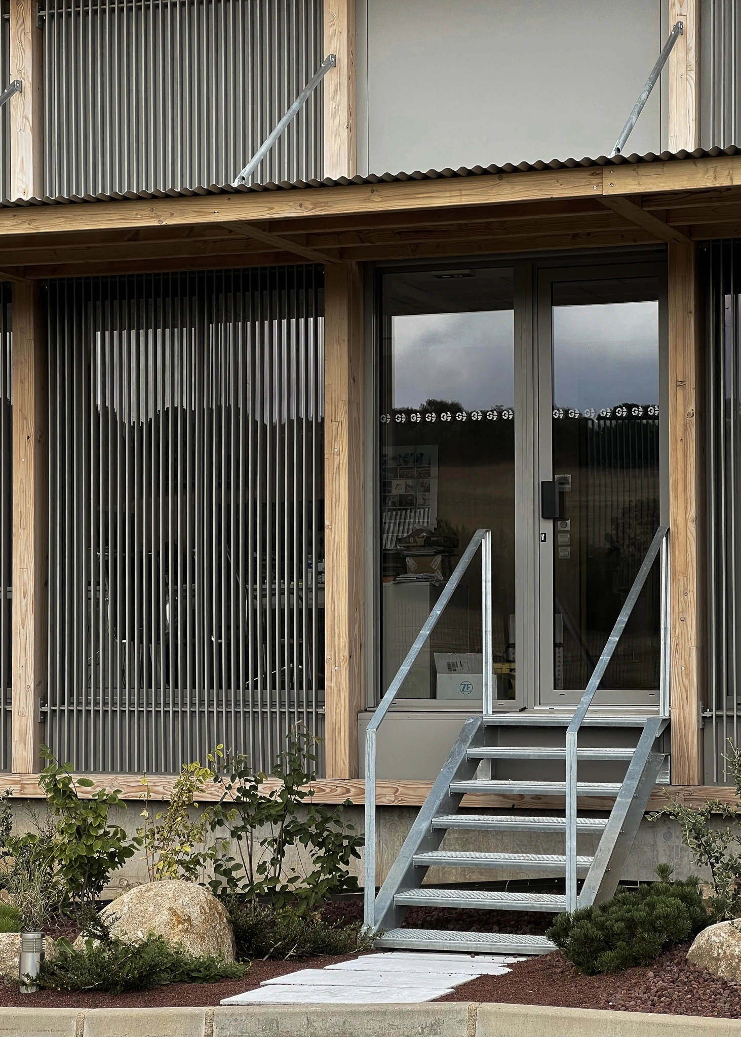 Façade du siège des Transports Galtier encadrée de bois et de brise-soleil métalliques, accessible par un escalier extérieur