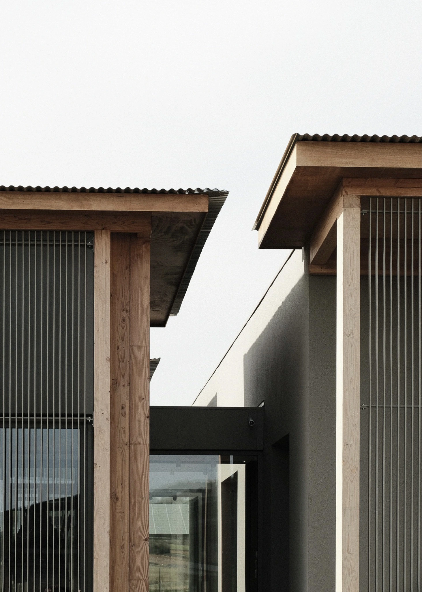 Jonction entre les volumes du siège des Transports Galtier, avec poteaux en bois, brise-soleil métalliques et toiture débordante.