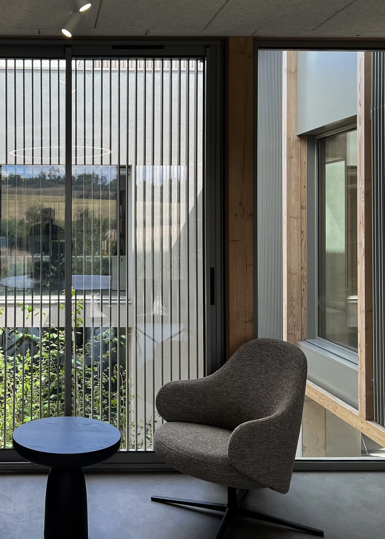 Espace d'attente dans la salle de réunion du siège des Transports Galtier avec fauteuil, table basse, baie vitrée et vue sur le patio